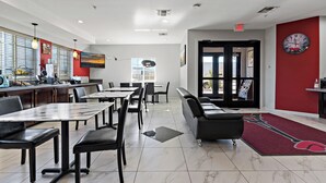 A modern dining area with marble flooring, black chairs, and tables. There is a red wall with a clock and a red carpet leading to the exit.