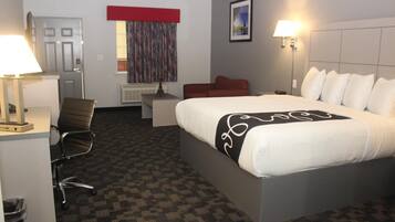 A hotel room with a large bed, a desk with a lamp, a chair, a red couch, and a painting on the wall.
