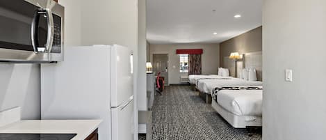A hotel room with a kitchenette, a bed with a headboard, a bedside table, and a lamp.