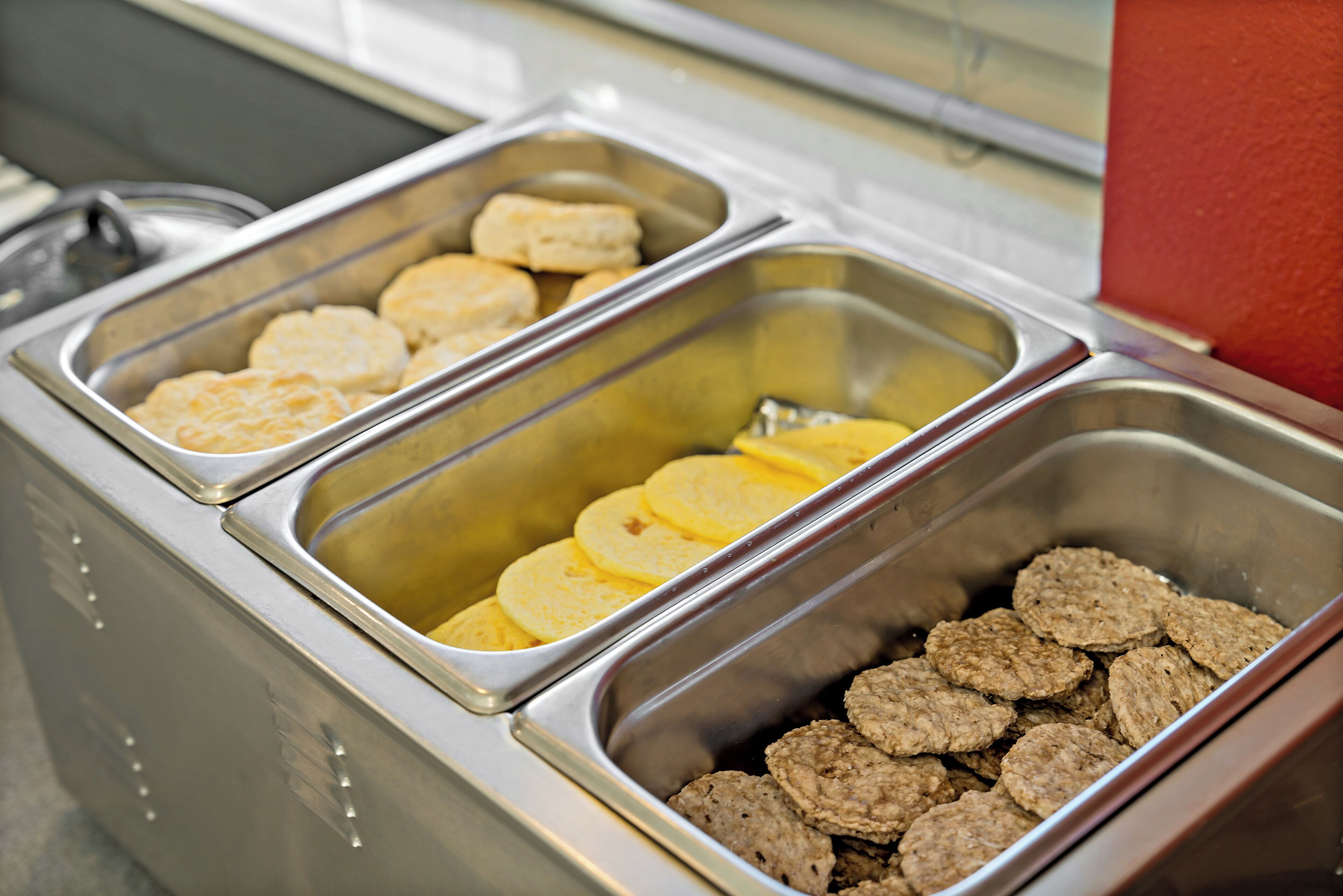 Un buffet avec trois plateaux de nourriture : des biscuits, des tranches de pommes de terre et des galettes de viande.
