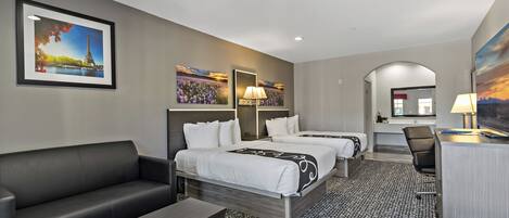 A hotel room with two beds, a sofa, a desk, and a chair. There are paintings on the walls and a view of the Eiffel Tower.