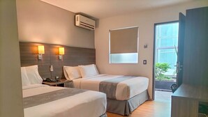 Habitación de hotel con dos camas, un escritorio, una silla, aire acondicionado y ventana con vistas al exterior.