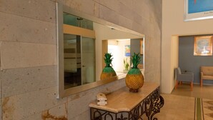 Un vestíbulo con un mostrador de recepción de mármol, dos jarrones con forma de piña, un espejo que refleja el interior y una obra de arte enmarcada en la pared.