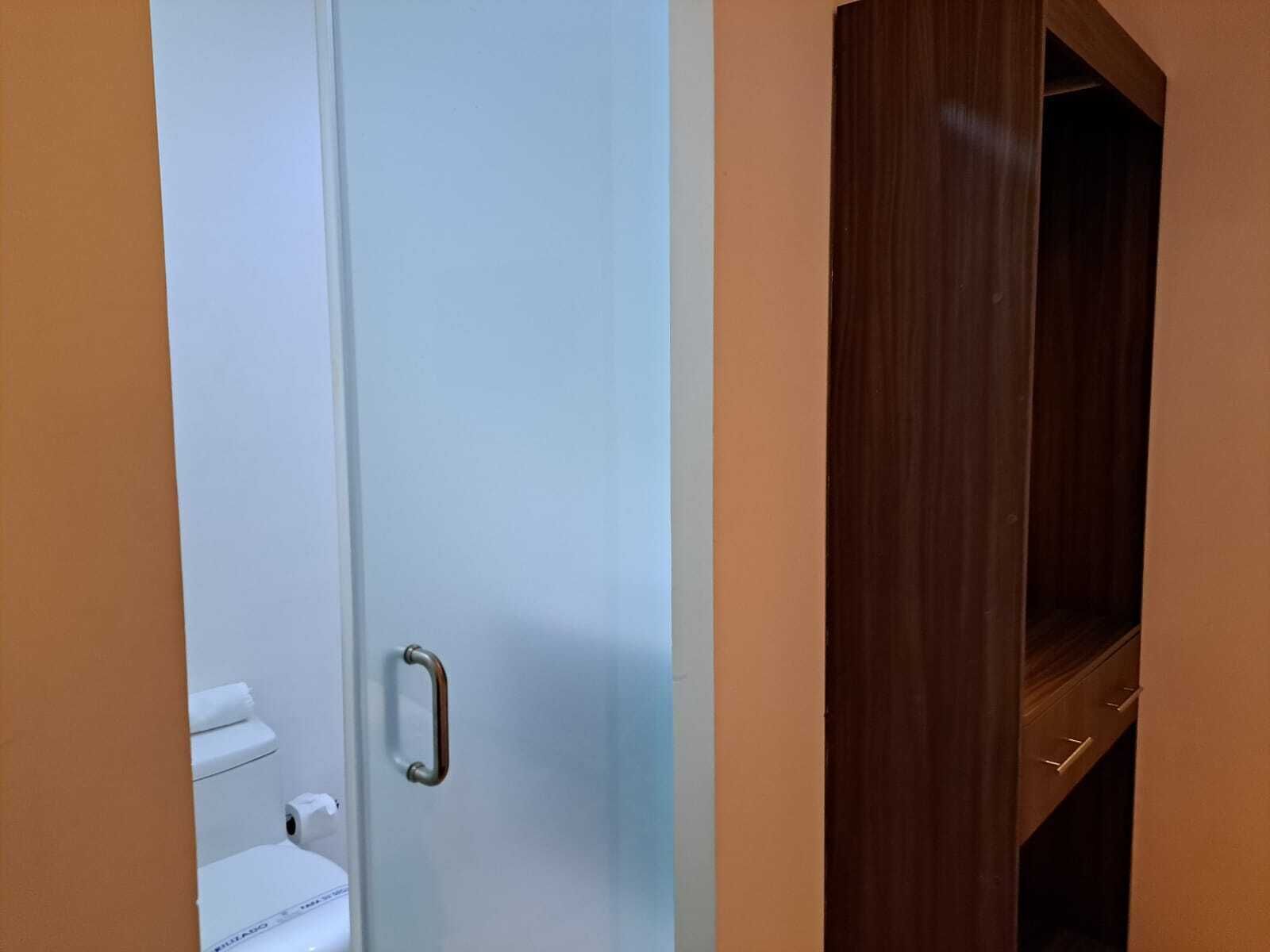 A bathroom with a white toilet, a roll of toilet paper, and a wooden cabinet with a handle.