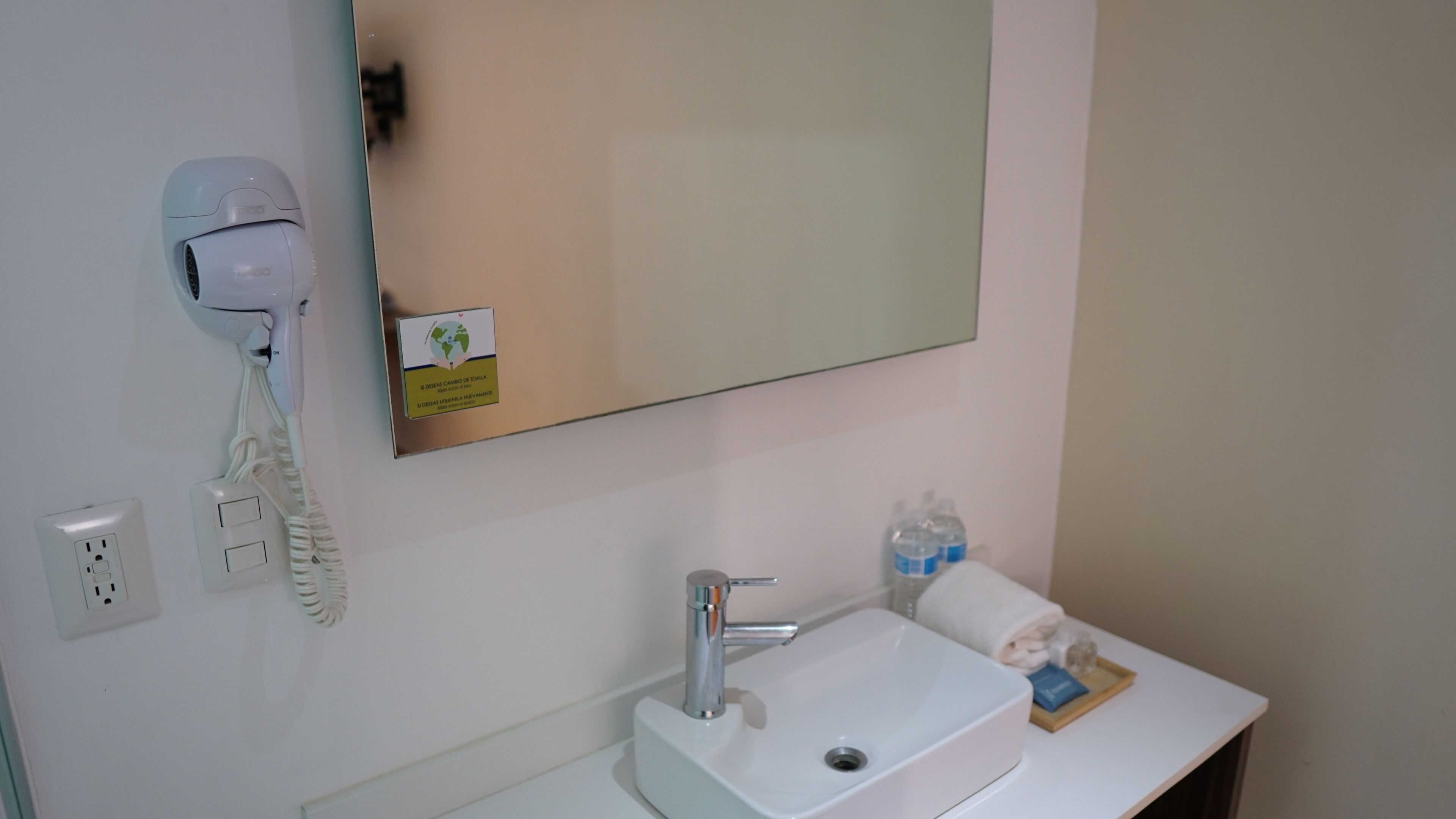 Une salle de bain avec un lavabo blanc, un miroir, un sèche-cheveux et des articles de toilette posés sur le comptoir.