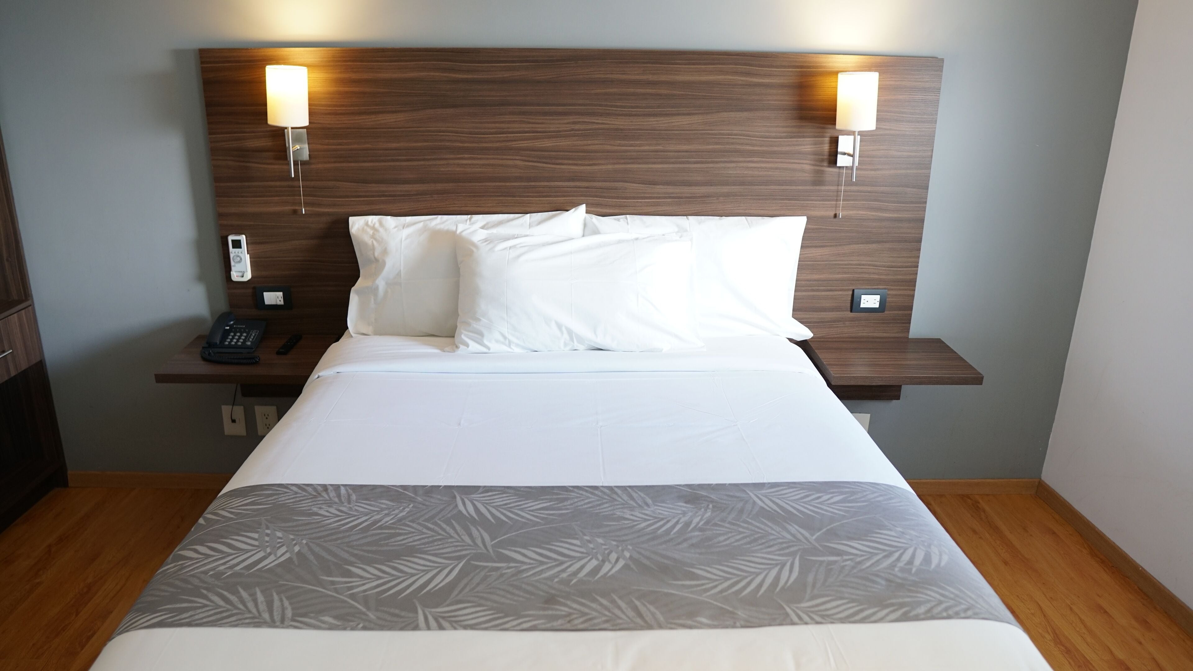 A neatly made bed with white linens, two bedside lamps, a phone, and a small table with a lamp.