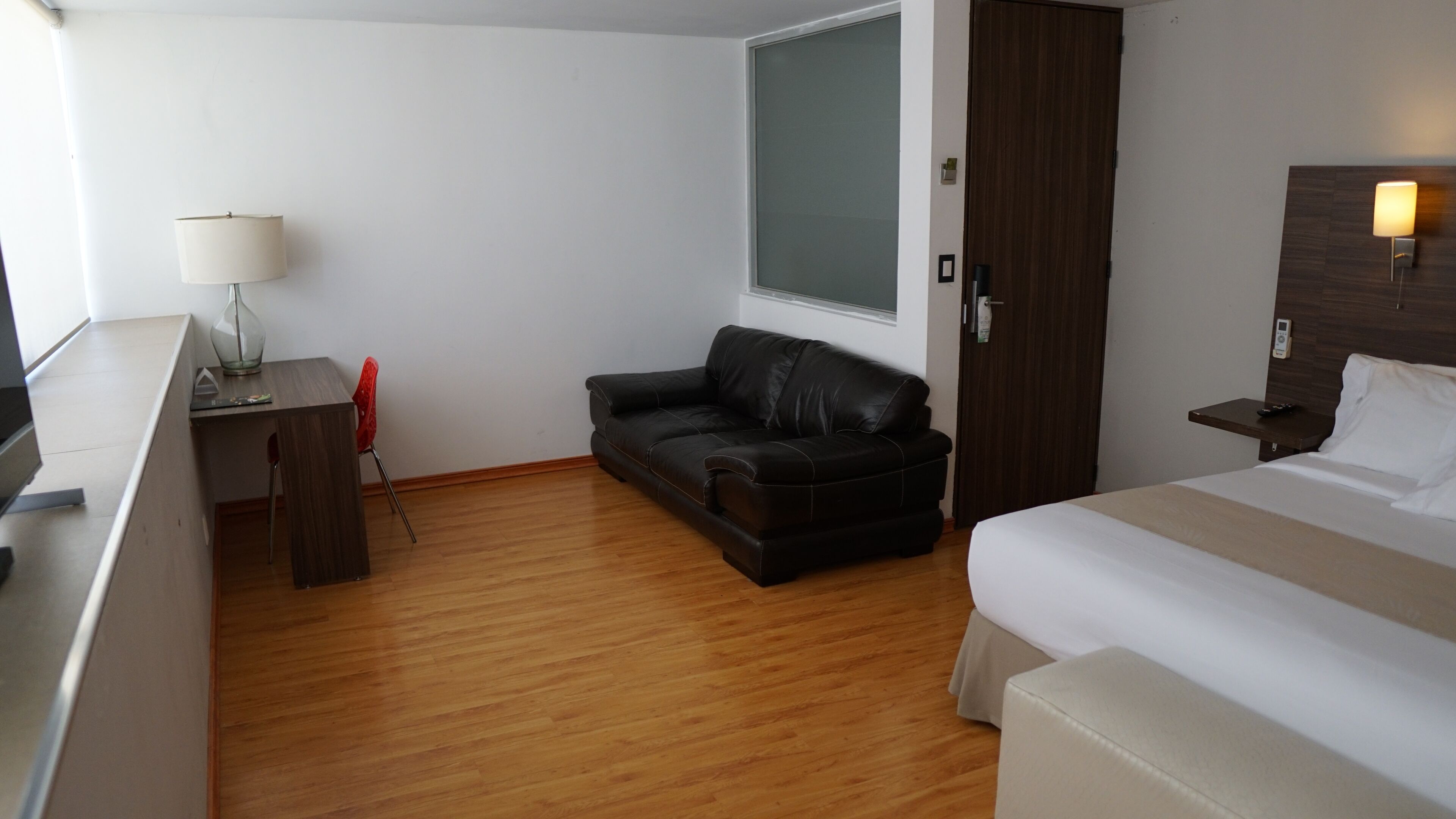 Une chambre d’hôtel avec un lit, un bureau doté d’une lampe, un canapé en cuir et un plancher en bois.