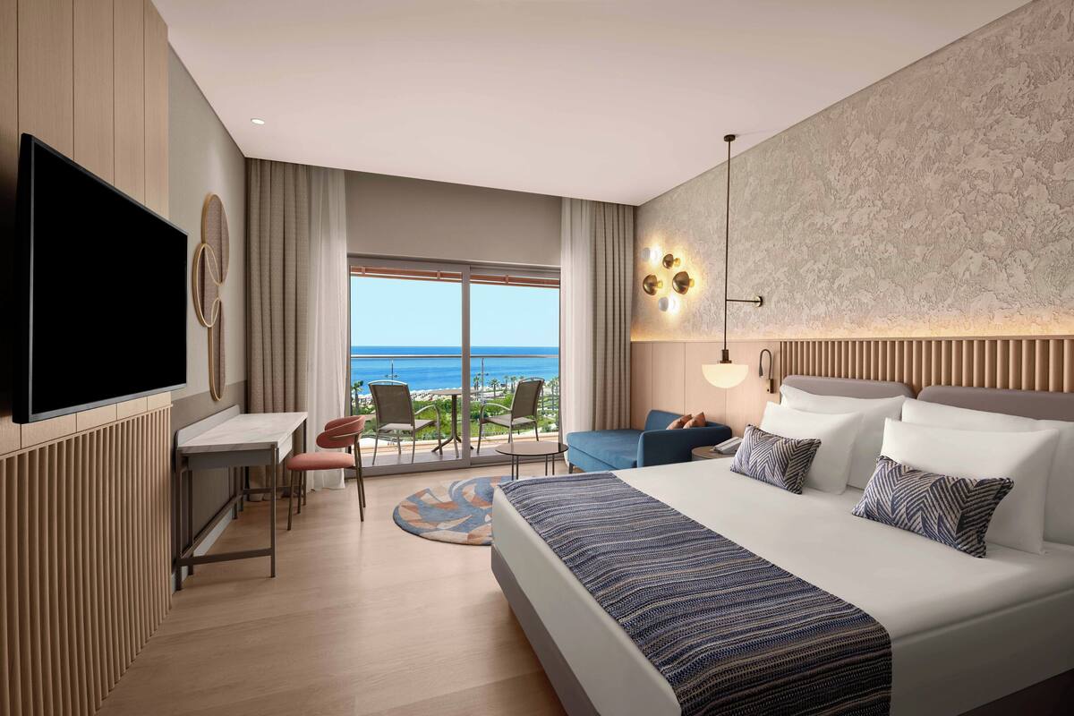 A modern hotel room with a large bed, a desk, and a view of the ocean.