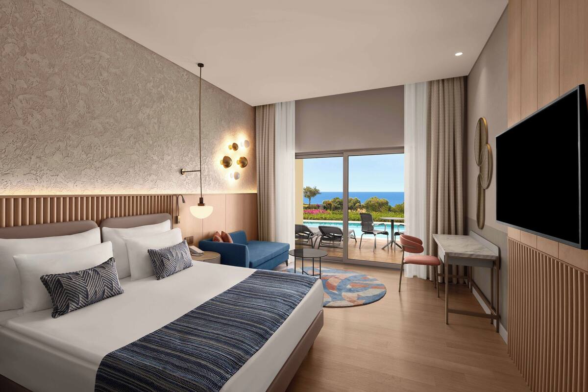 A modern hotel room with a large bed, a desk, and a view of the ocean.