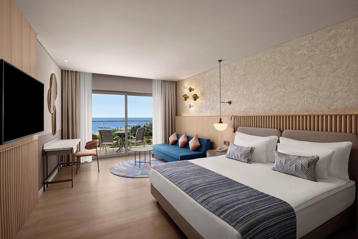Habitación de hotel moderna con una cama grande, un escritorio, una televisión y un balcón con vistas.