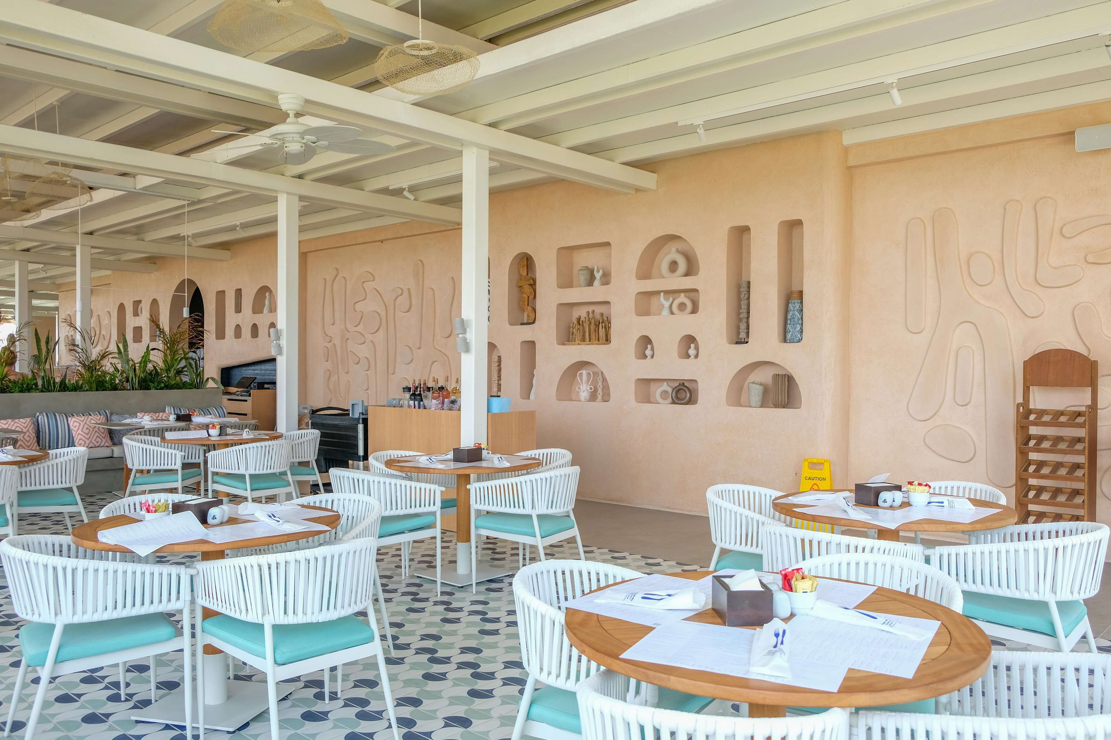 An outdoor seating area with white wicker chairs and tables, a bar area, and decorative wall art.