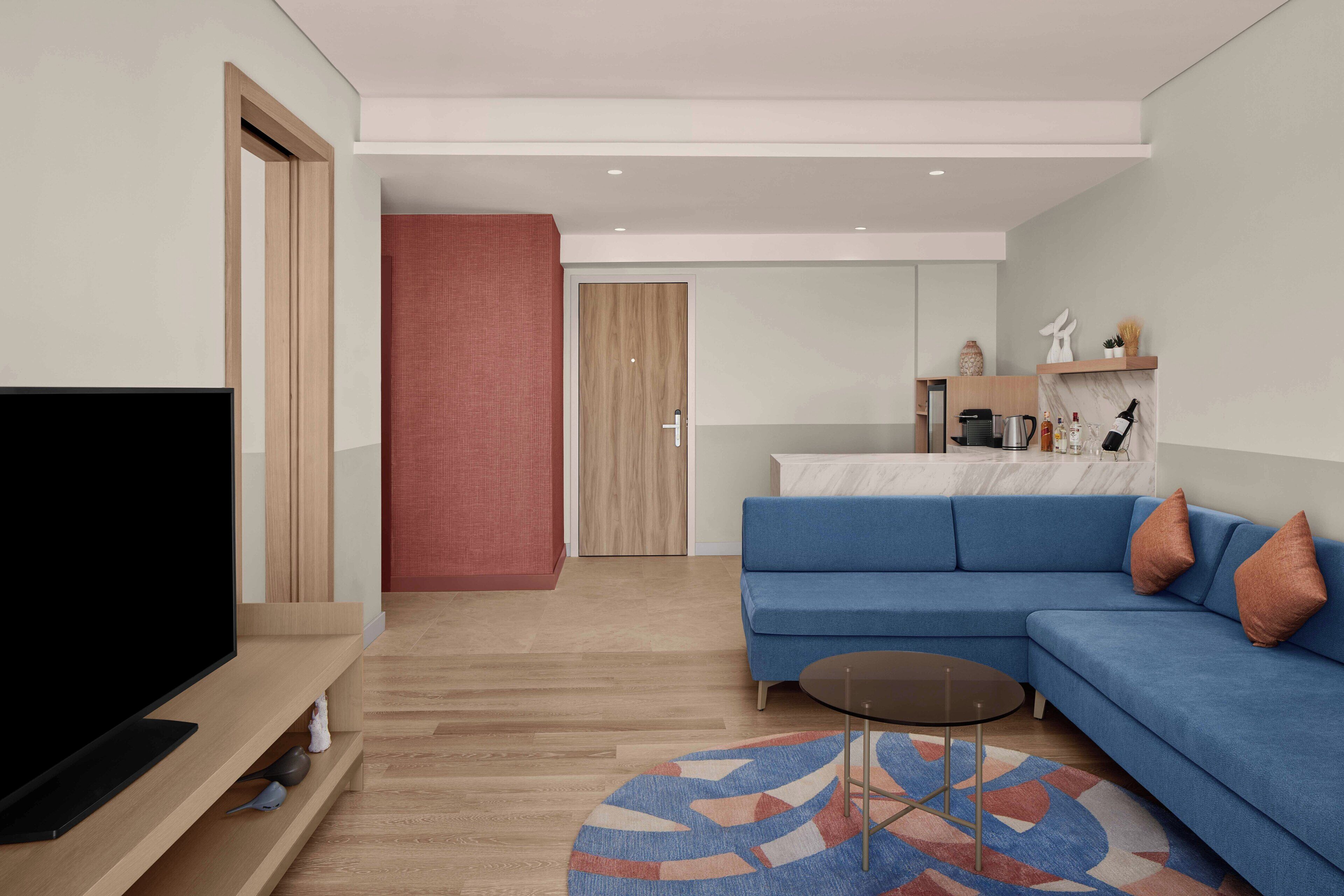A modern living room with a flat-screen TV, a blue sofa, a coffee table, and a patterned rug.