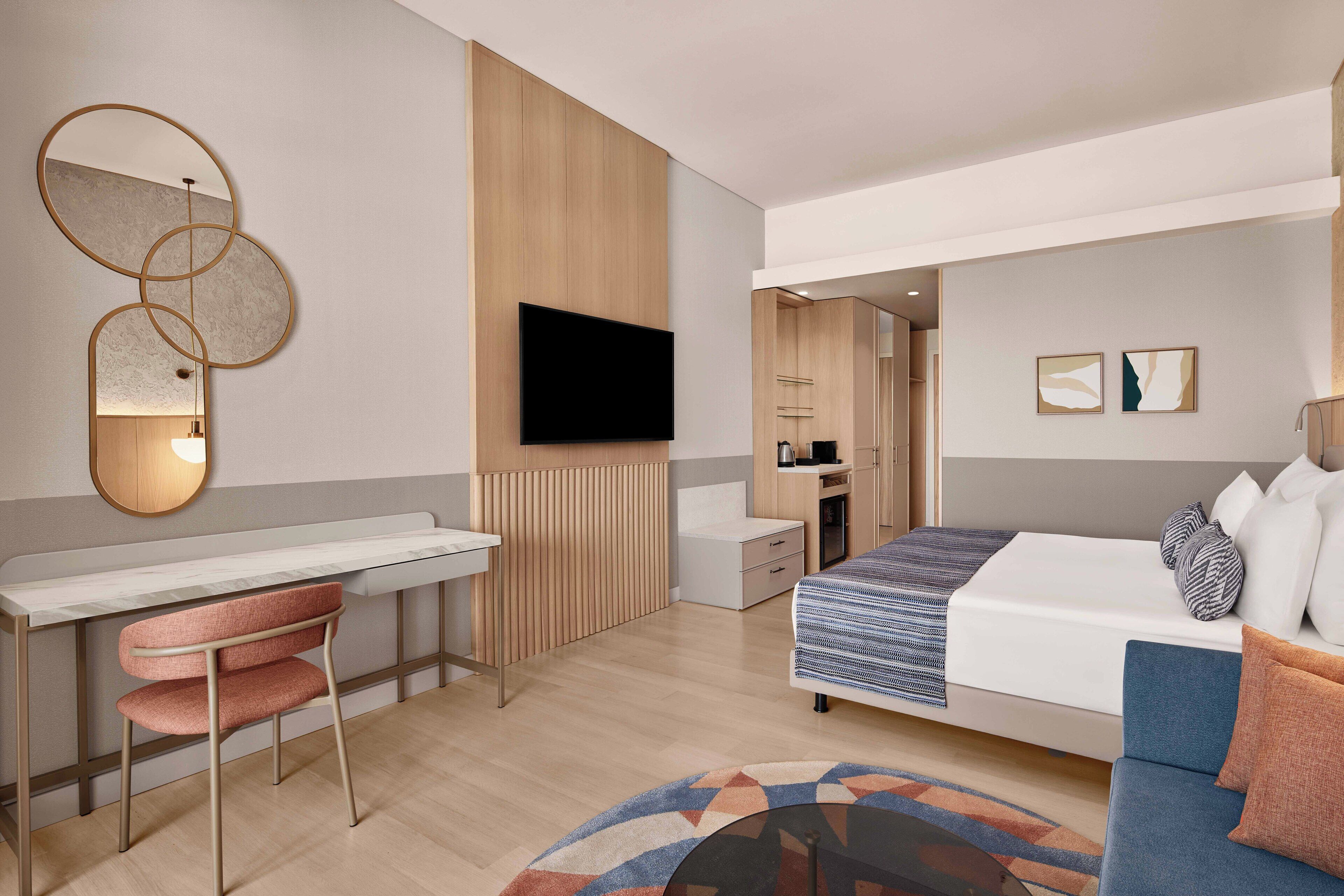 Una camera d'albergo moderna con un letto, una scrivania, una sedia, una TV e un bagno piccolo.