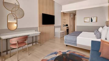 Una camera d'albergo moderna con un letto, una scrivania, una sedia, una TV e un bagno piccolo.