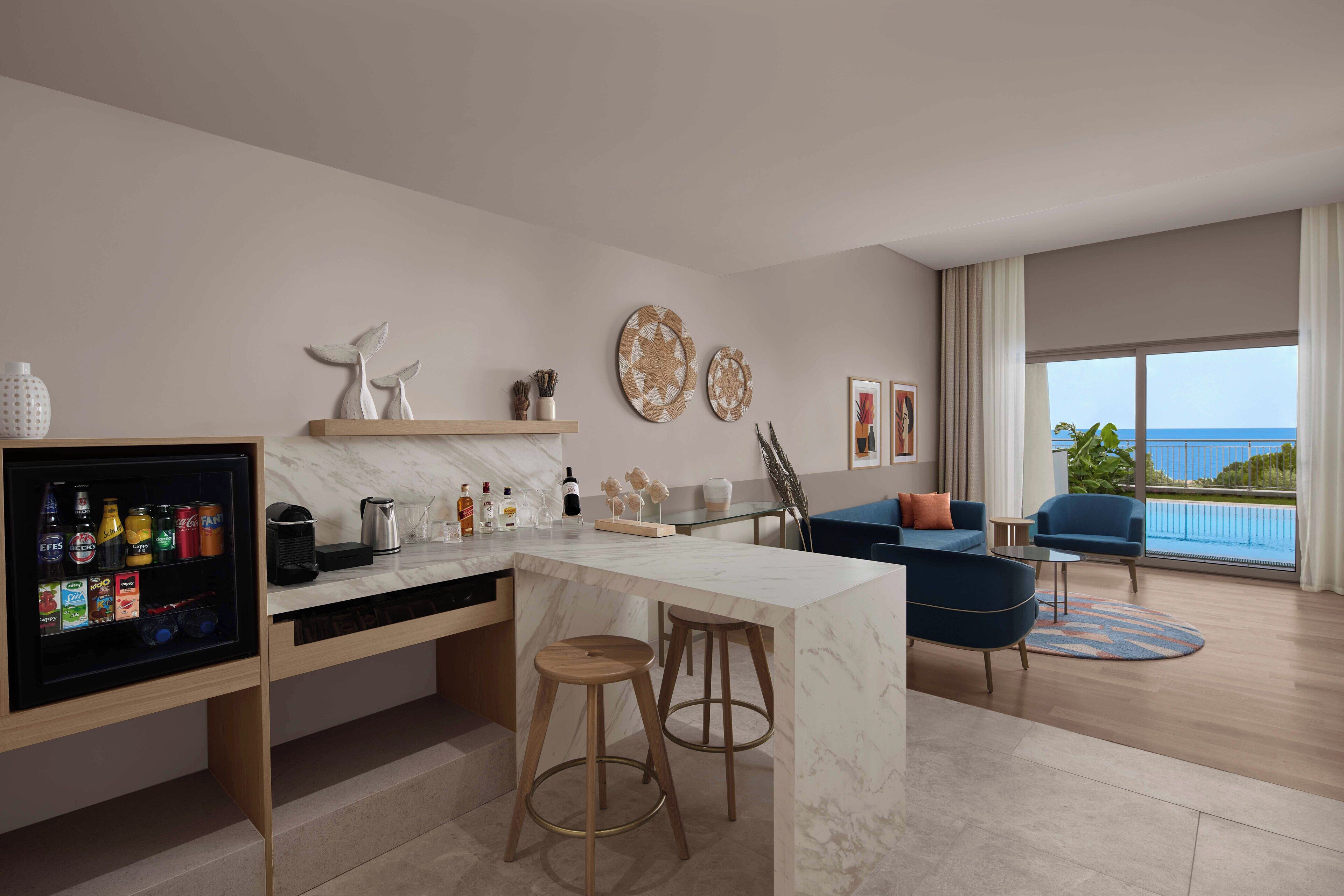 A modern living room with a marble island, bar stools, a sofa, and a view of the ocean.