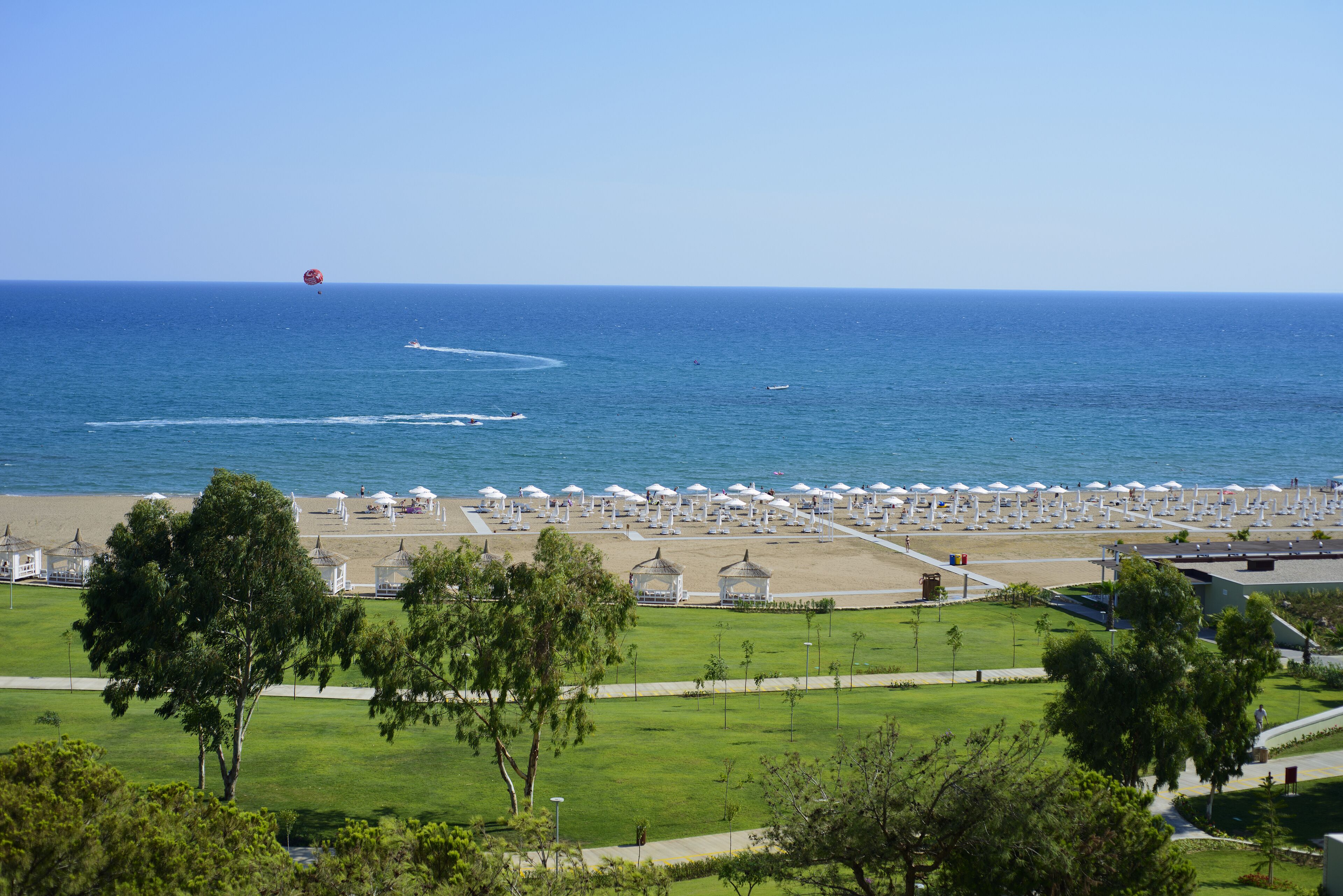 Un complejo turístico en la playa con una amplia zona de arena, numerosas sombrillas blancas y una vista despejada del océano.
