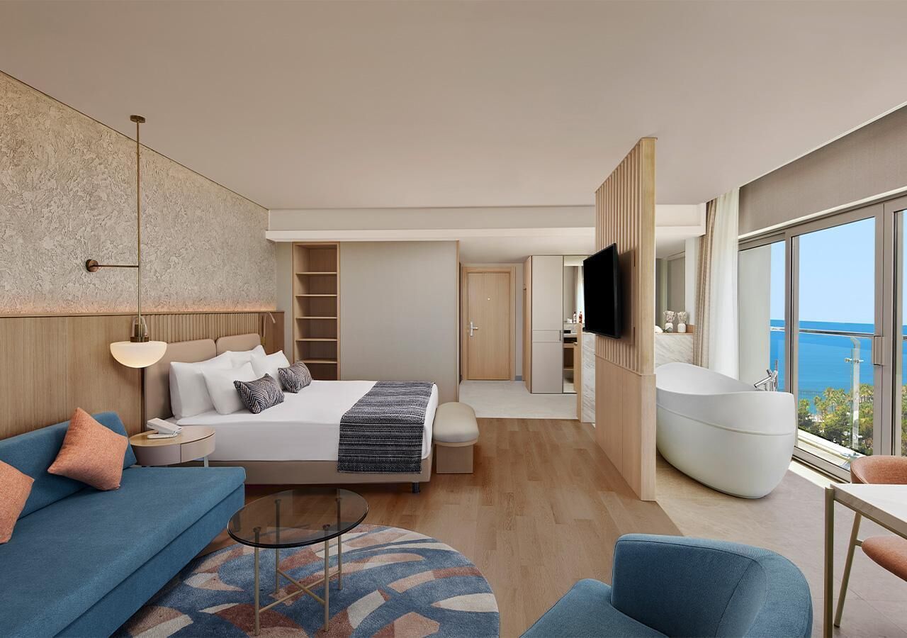 Ein modernes Hotelzimmer mit Bett, Sofa, Fernseher und einem großen Fenster mit Blick.