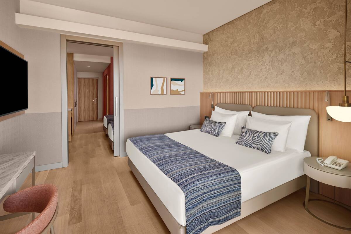 A modern hotel room with a large bed, bedside table, and a TV mounted on the wall.