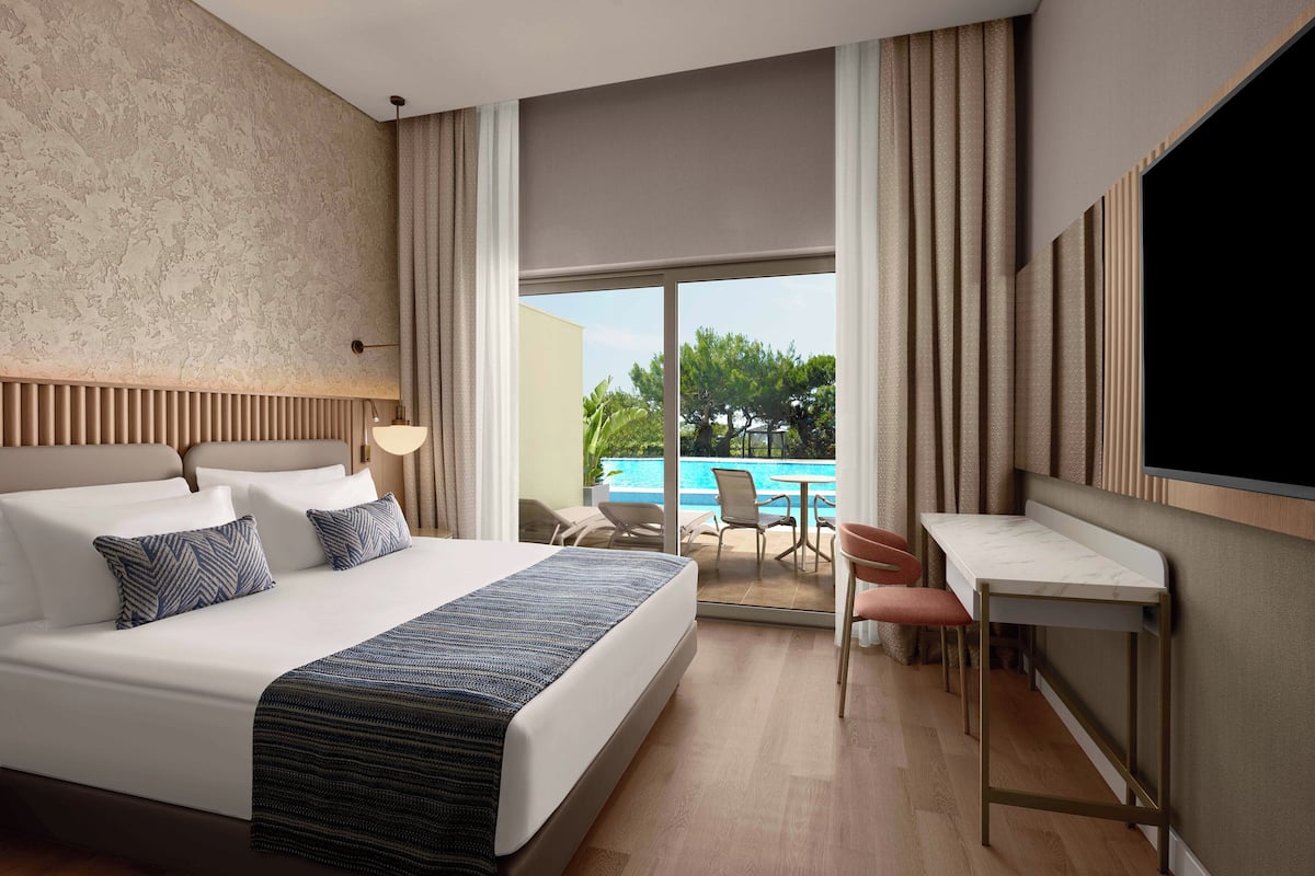 A hotel room with a large bed, a desk, and a view of a swimming pool.