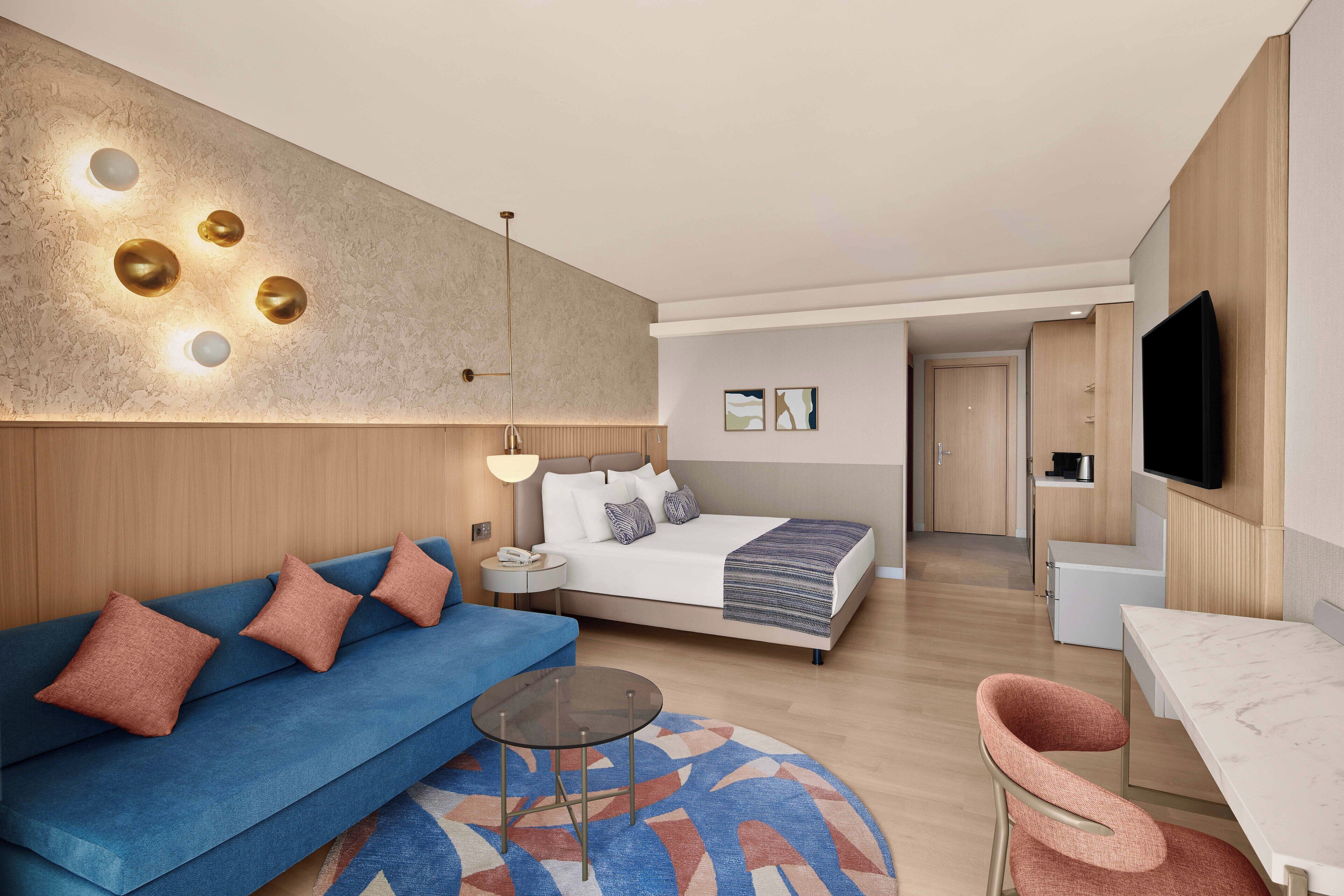 A modern hotel room with a sofa, a bed, a TV, and a dining area.