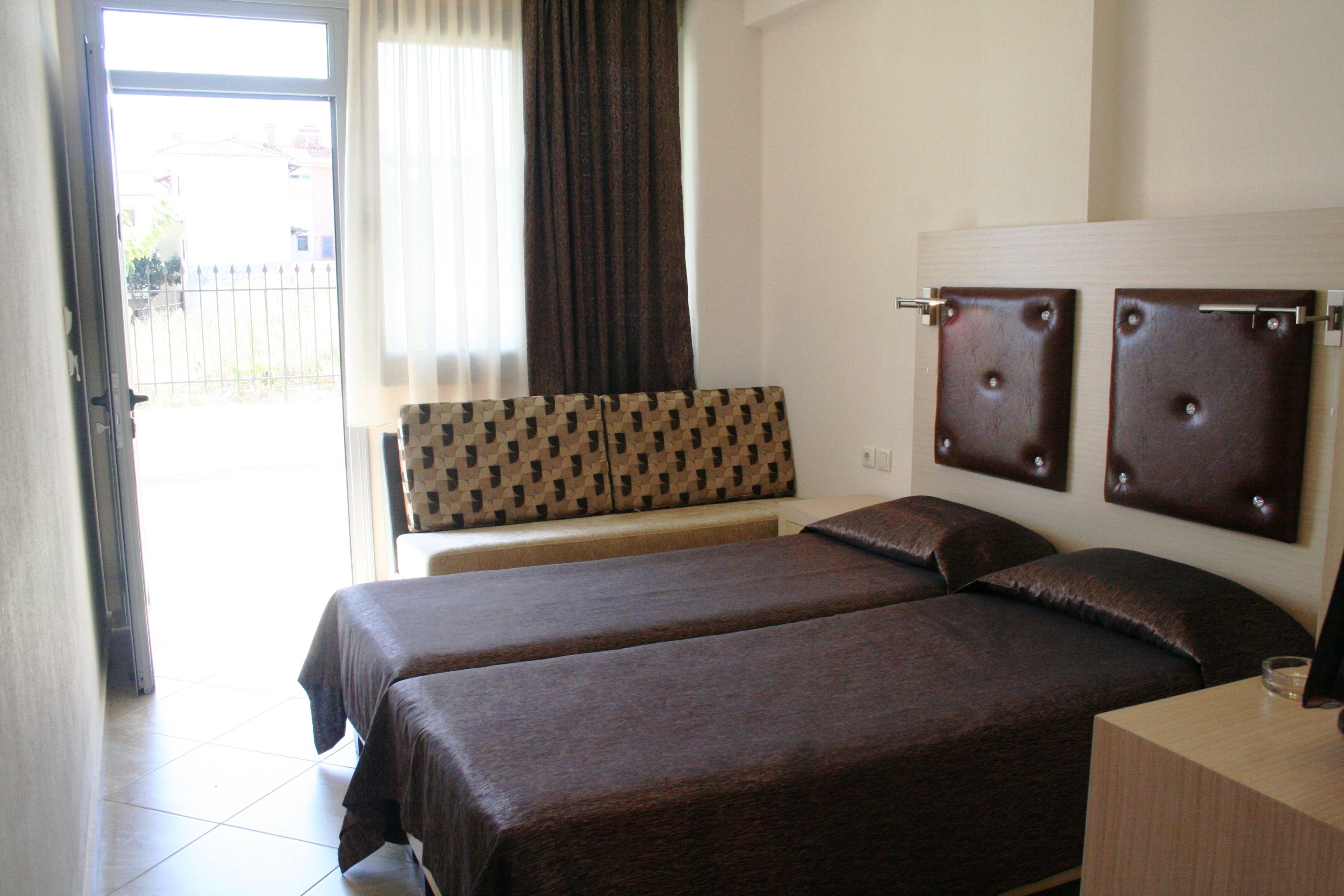 Habitación de hotel con dos camas, un banco, una ventana con cortinas y vistas al exterior.