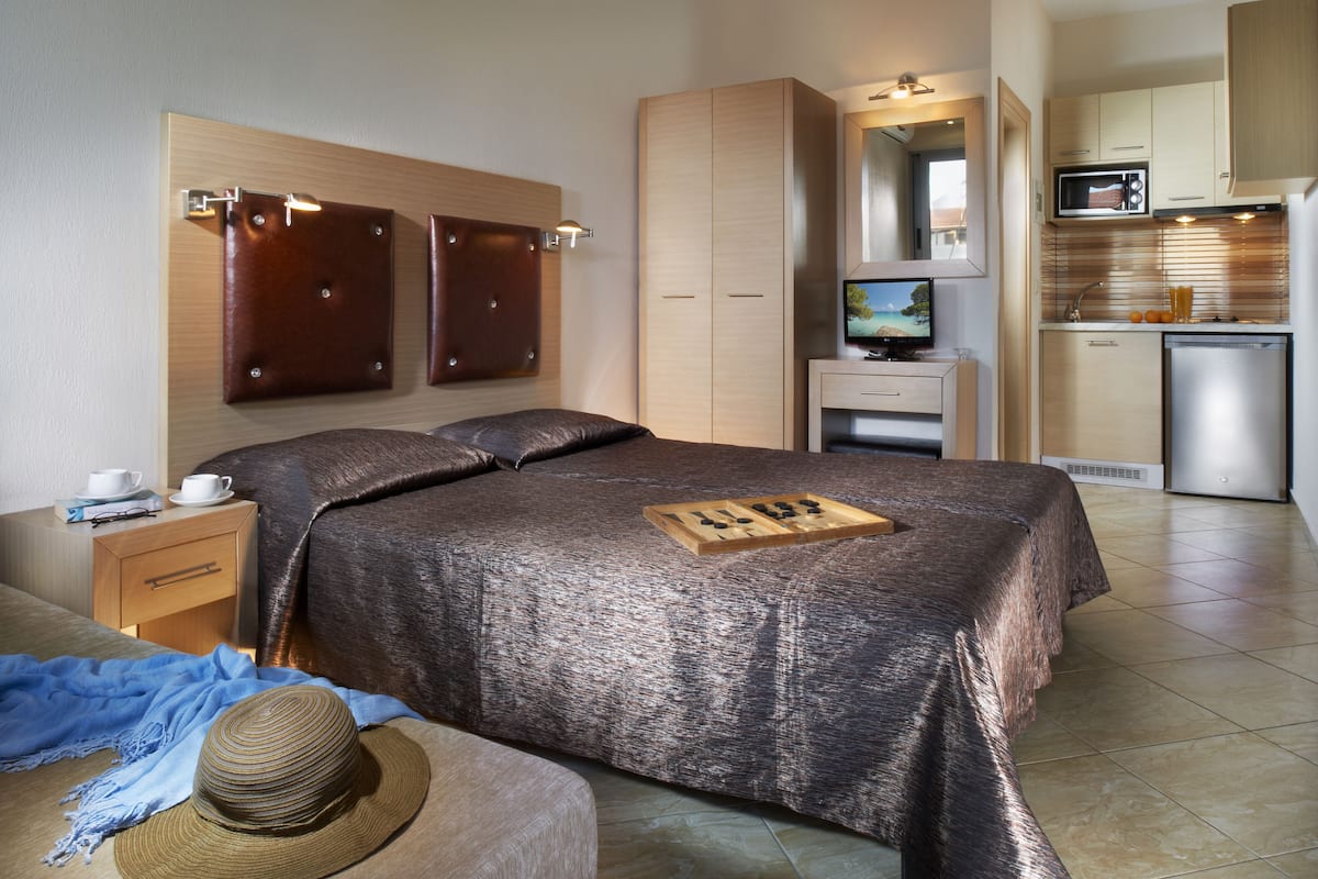 A modern hotel room with a large bed, a small desk, a television, and a kitchenette.
