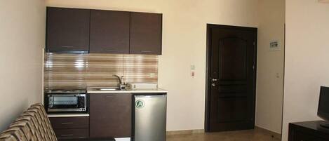 A compact kitchen with dark cabinets, a built-in oven, and a compact refrigerator.