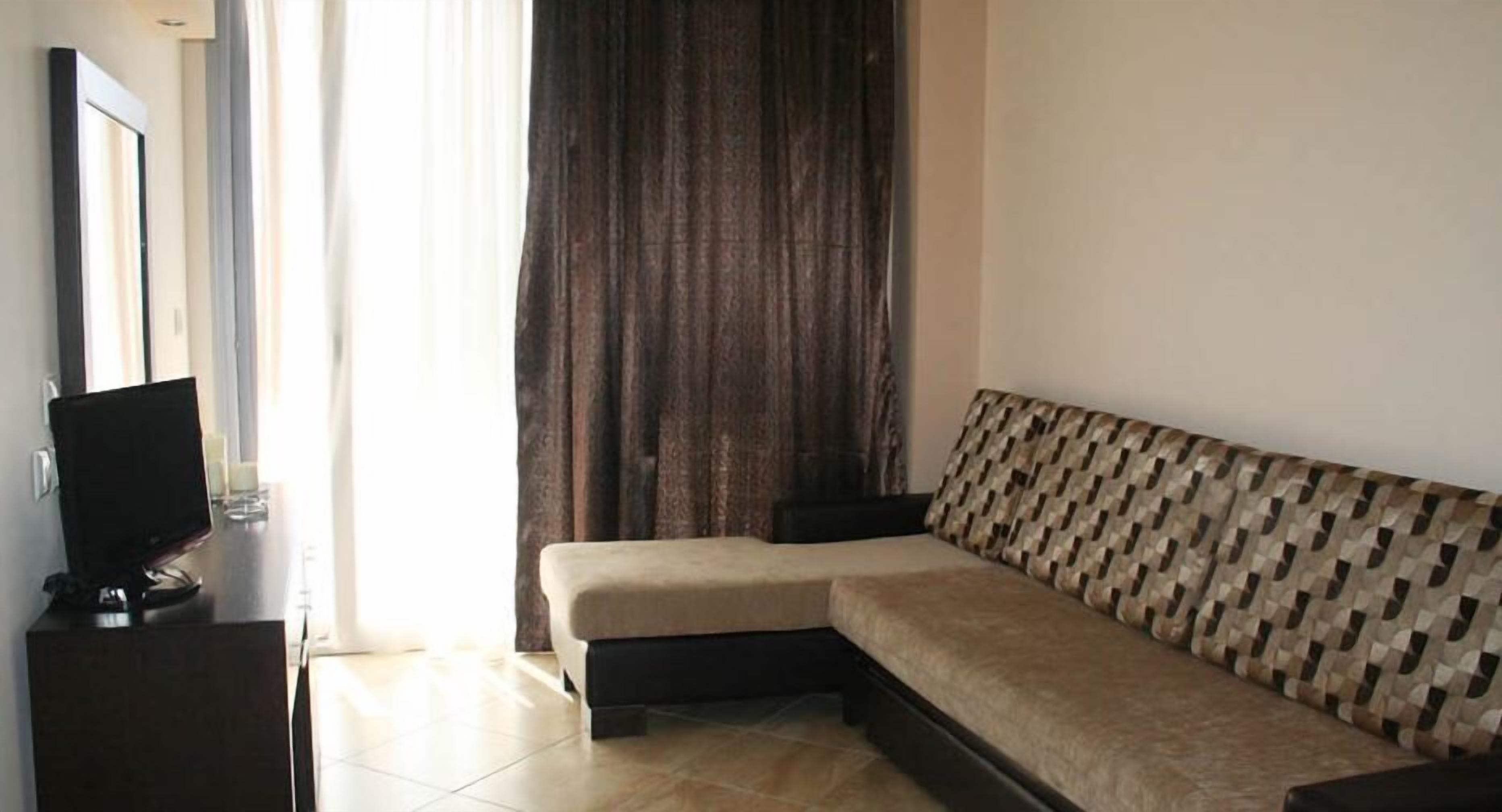 A modern living room with a sofa, a flat-screen TV, and a large window with curtains.