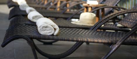 Une rangée de fauteuils de jardin en osier, avec des serviettes et des chapeaux soigneusement disposés.