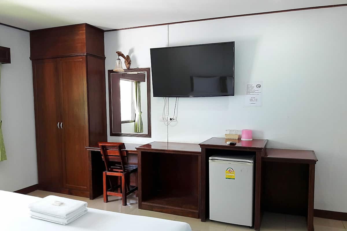 A hotel room with a bed, a desk, a chair, a wardrobe, a television, and a mini-fridge.