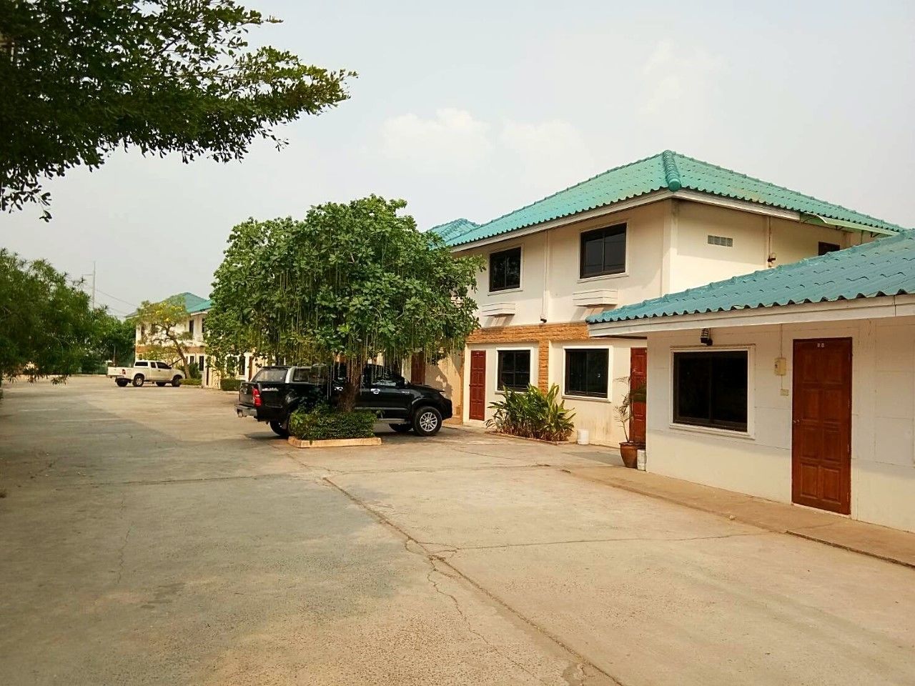 A two-story building with a green roof, parked vehicles, and a paved driveway.