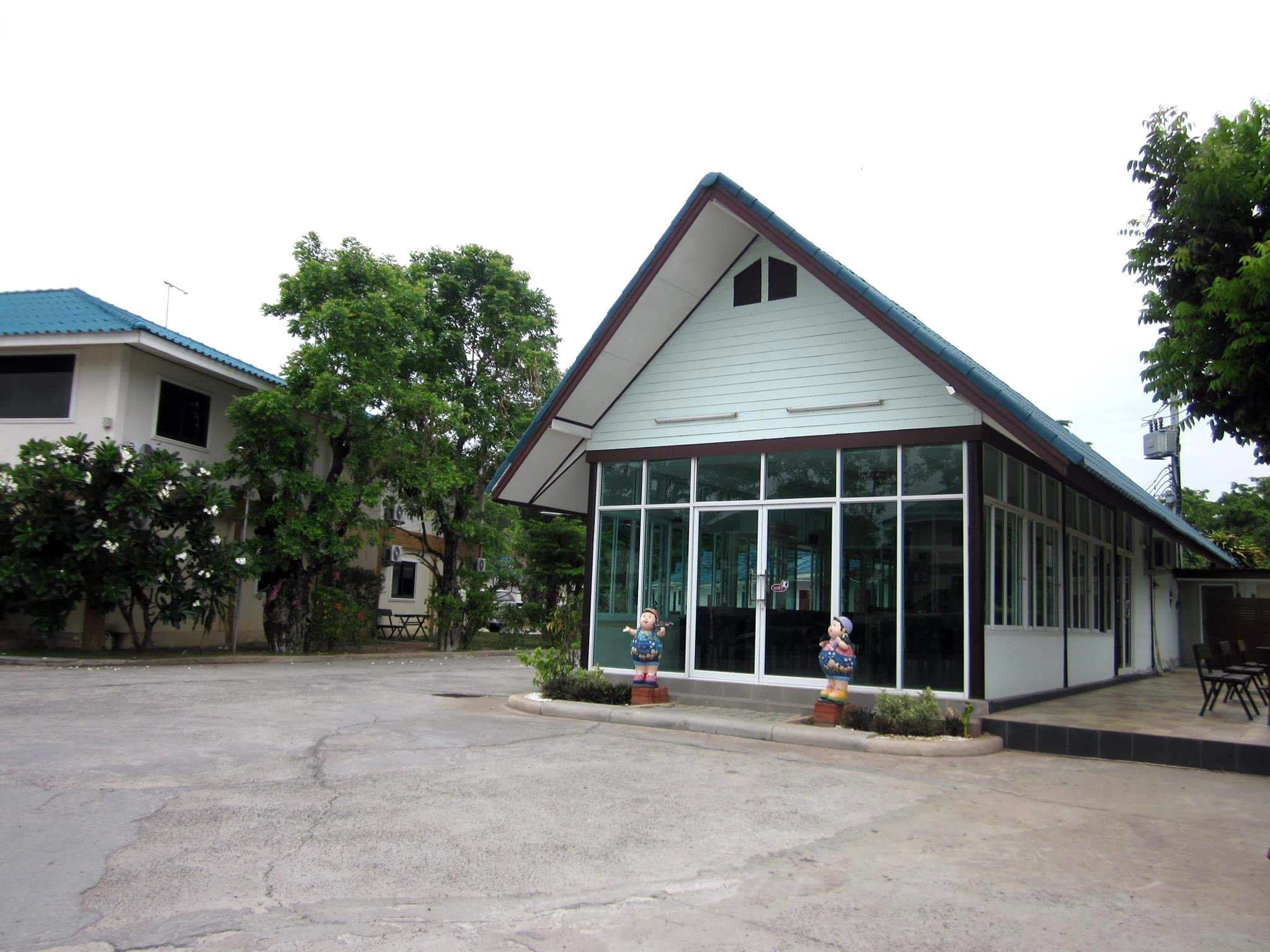 A building with a pitched roof and large windows, surrounded by trees and a parking lot.
