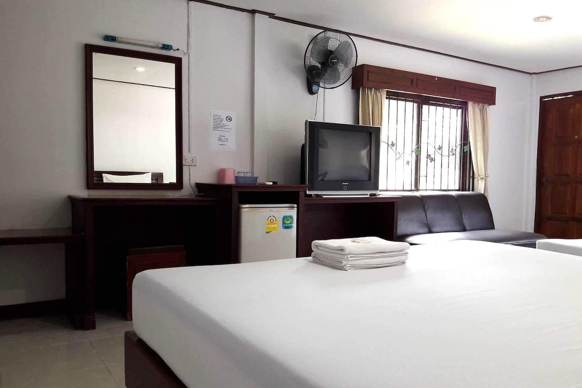 A hotel room with a bed, a desk, a television, a refrigerator, and a window with curtains.
