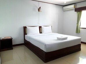 A neatly made bed with white linens, a wooden headboard, and a nightstand with a telephone and a magazine.