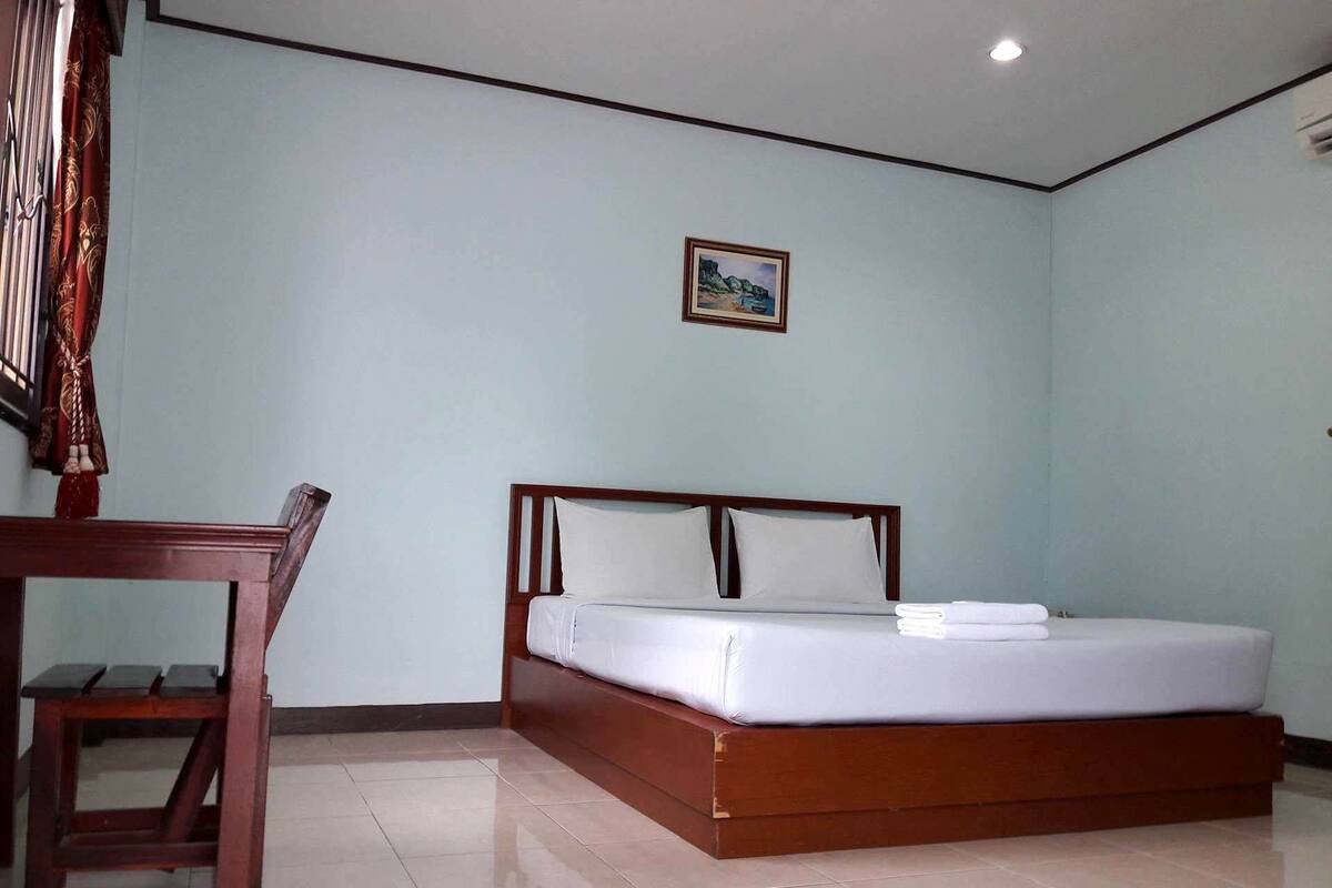 A neatly arranged bedroom with a wooden bed, a small table, and a picture on the wall.