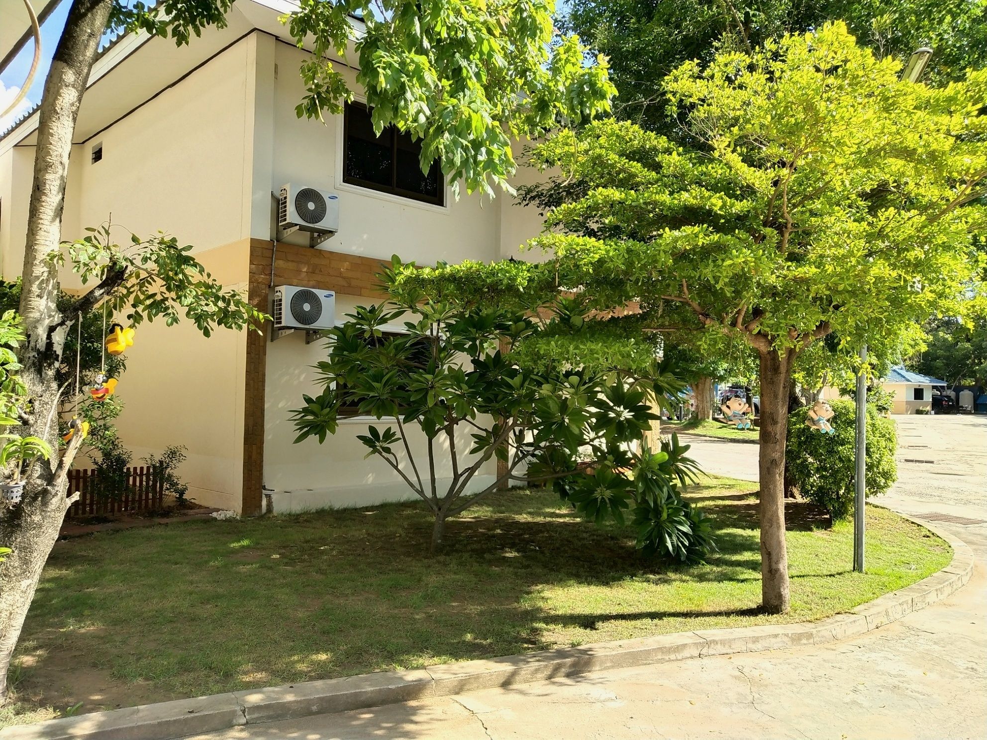 A building with a flat roof, air conditioning units, and a well-maintained lawn with various trees and shrubs.
