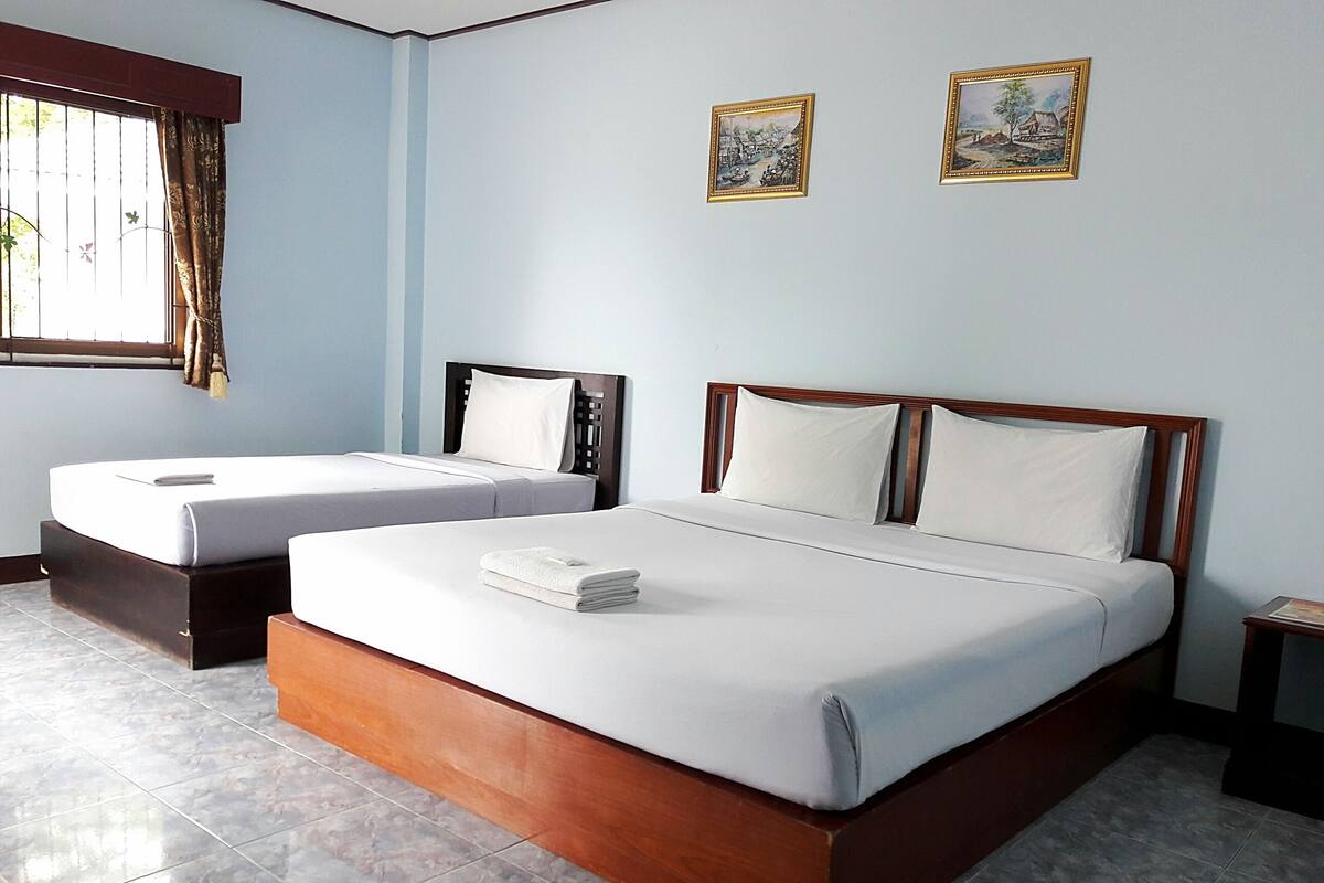 A hotel room with two single beds and a larger bed, all with wooden frames and white bedding.