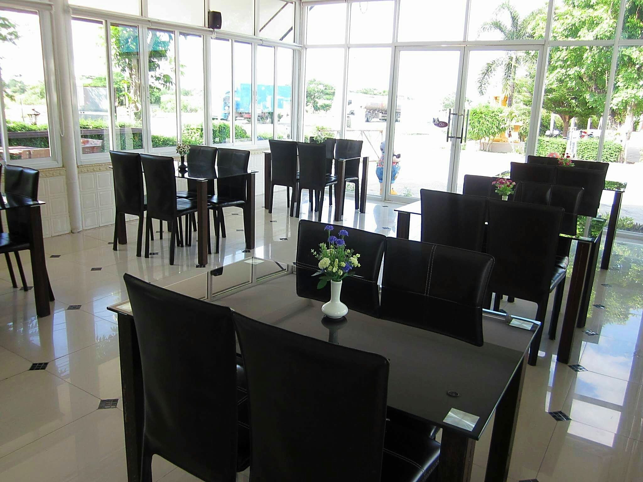 A spacious indoor area with large windows, black chairs, and tables arranged for dining or meetings.