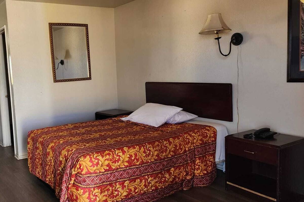 A hotel room with a bed, bedside table, lamp, and a mirror on the wall.