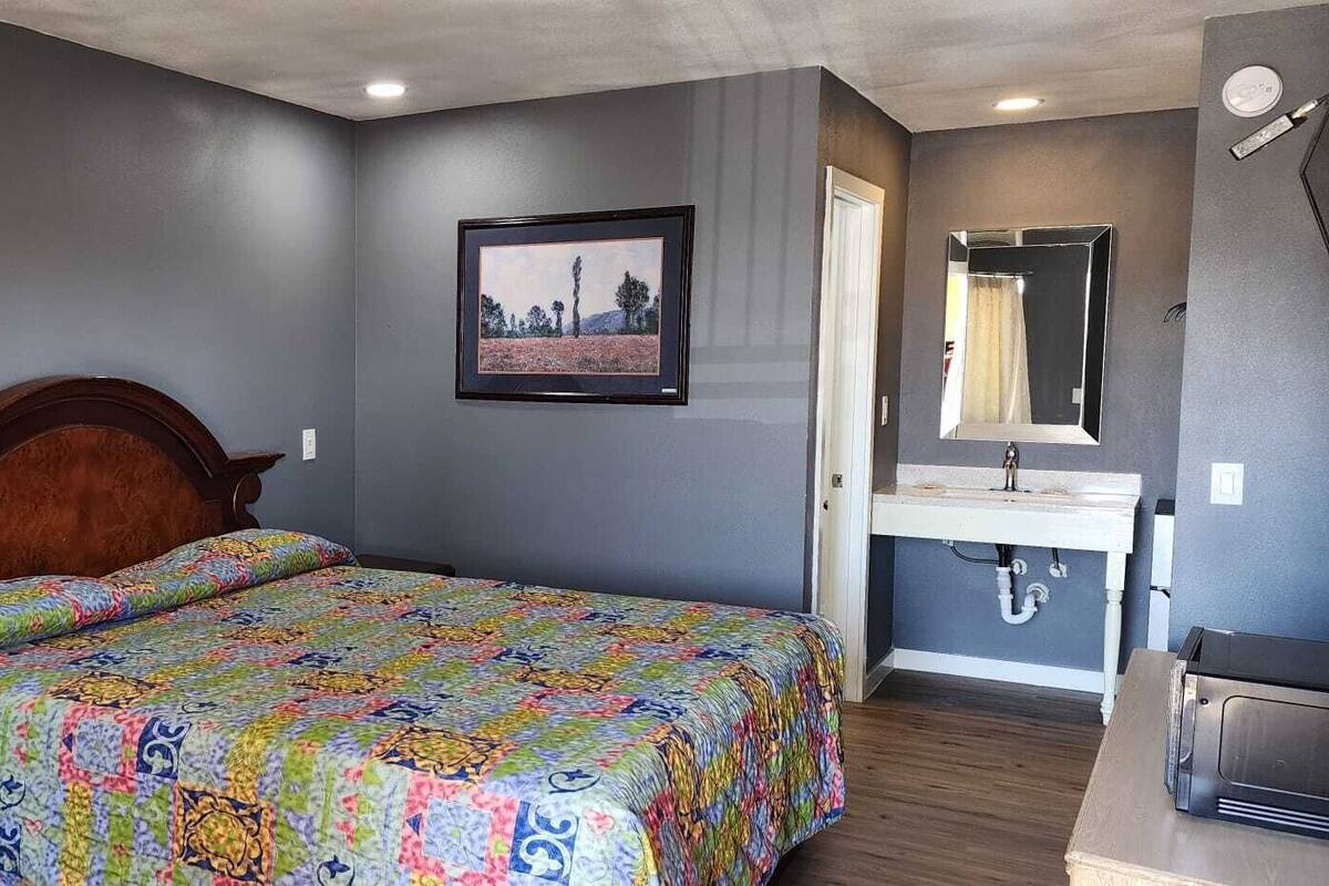 A bedroom with a wooden bed, a bedside table, a nightstand, a dresser, a bathroom with a sink and mirror, and two framed pictures on the wall.