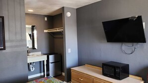 A compact room with a kitchenette, a microwave, a TV mounted on the wall, and a small wooden dresser. - Economy Inn Victorville (Victorville)