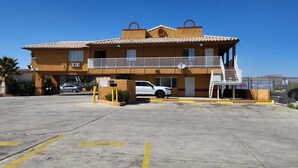 A two-story building with a balcony, a parking lot, and a fenced area with a sign. - Economy Inn Victorville (Victorville)