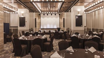 A conference room with multiple tables and chairs, a large screen at the front, and a modern ceiling design.