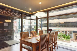 A modern dining area with a large table and chairs, large windows offering a view of the cityscape. - Hotel Uri& (Seoul)