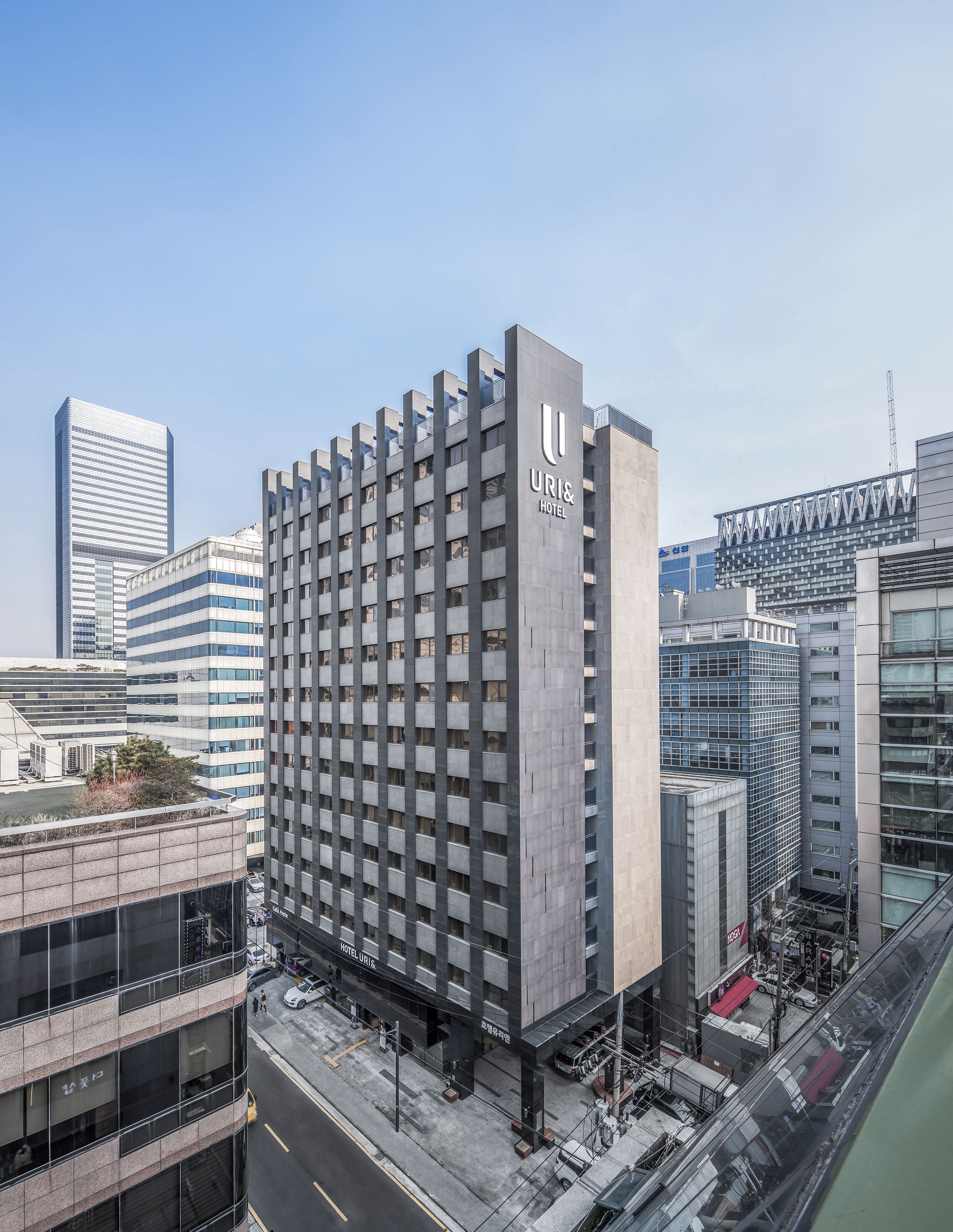 A modern hotel building with a prominent 'URI & HOTEL' sign, featuring a grid-like facade and multiple floors.