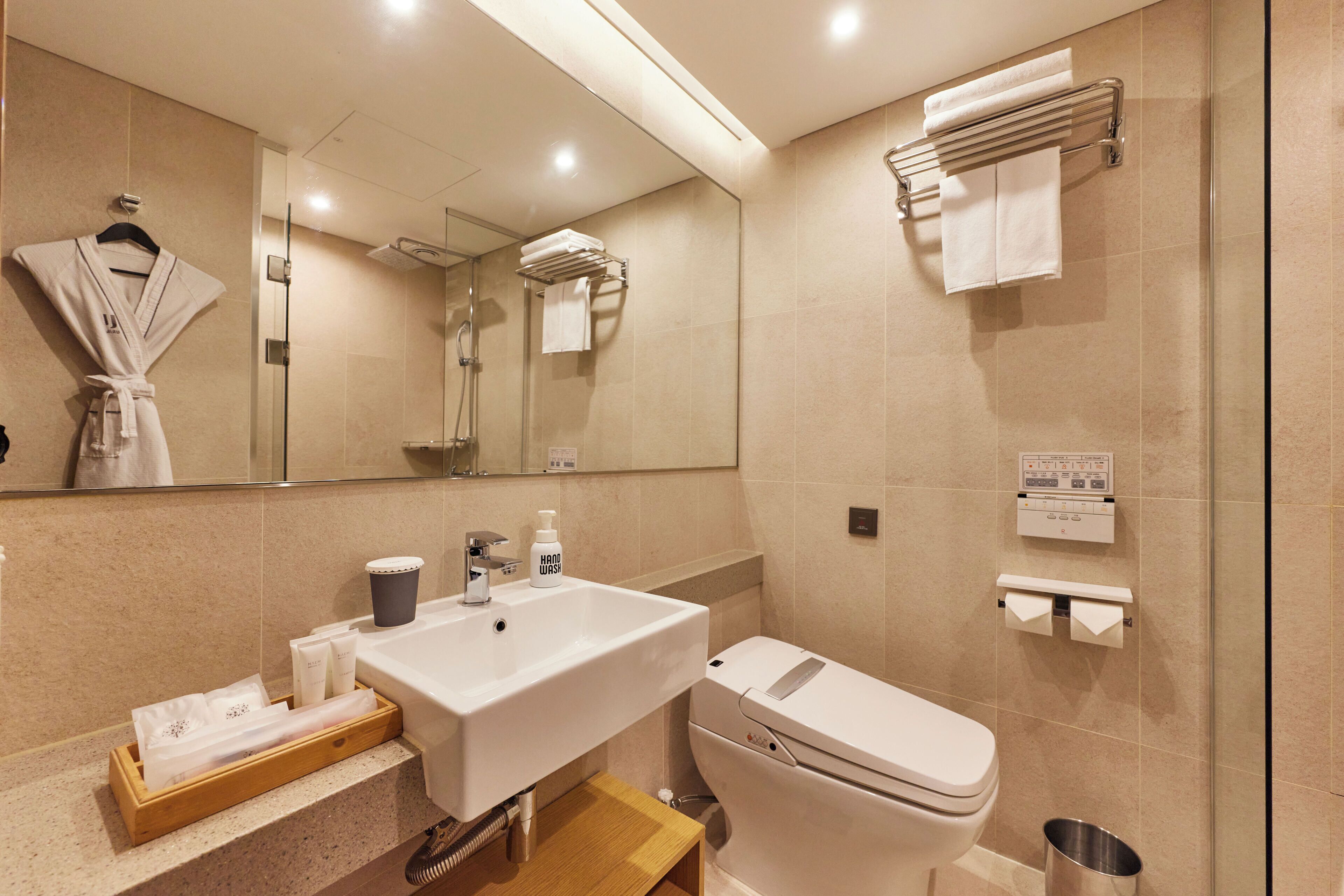 Un baño moderno con lavamanos, inodoro y ducha. Hay toallas y artículos de aseo en la encimera.