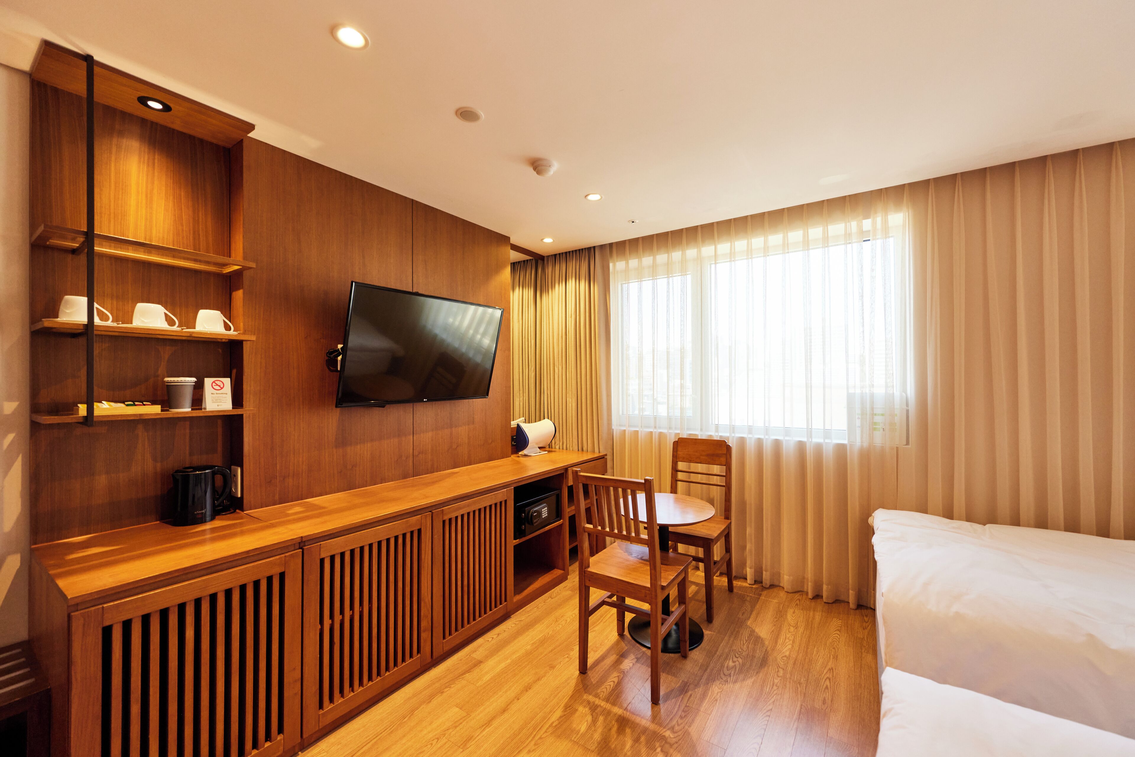 A hotel room with a wooden desk, a flat-screen TV, a dining table with chairs, and a bed.