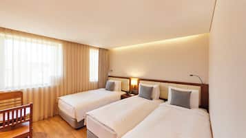 A hotel room with two single beds, a wooden chair, a desk, and a window with curtains.