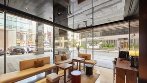 Un interior modern amb zones d'estar, una taula de treball i grans finestres que donen a la vista del carrer.