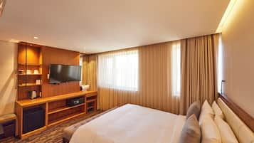 A hotel room with a large bed, a flat-screen TV, a wooden desk, and a minibar.